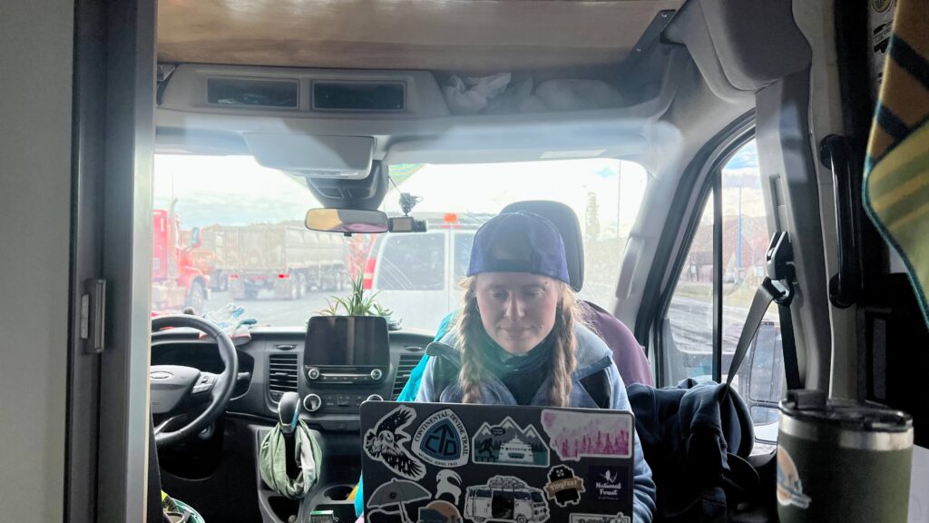Woman blogging in the swiveled front seat of a converted van at the beet harvest.