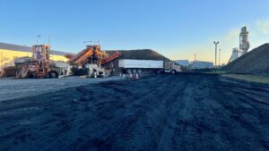 A beet piler piling beets while a dump truck gets stuck in the mud.
