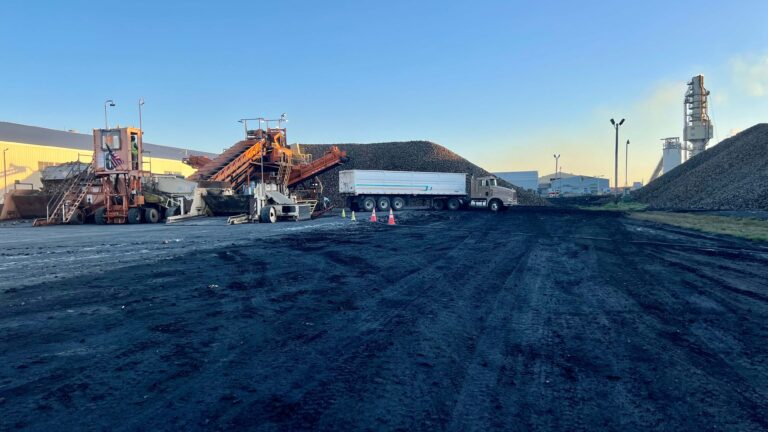 A beet piler piling beets while a dump truck gets stuck in the mud.