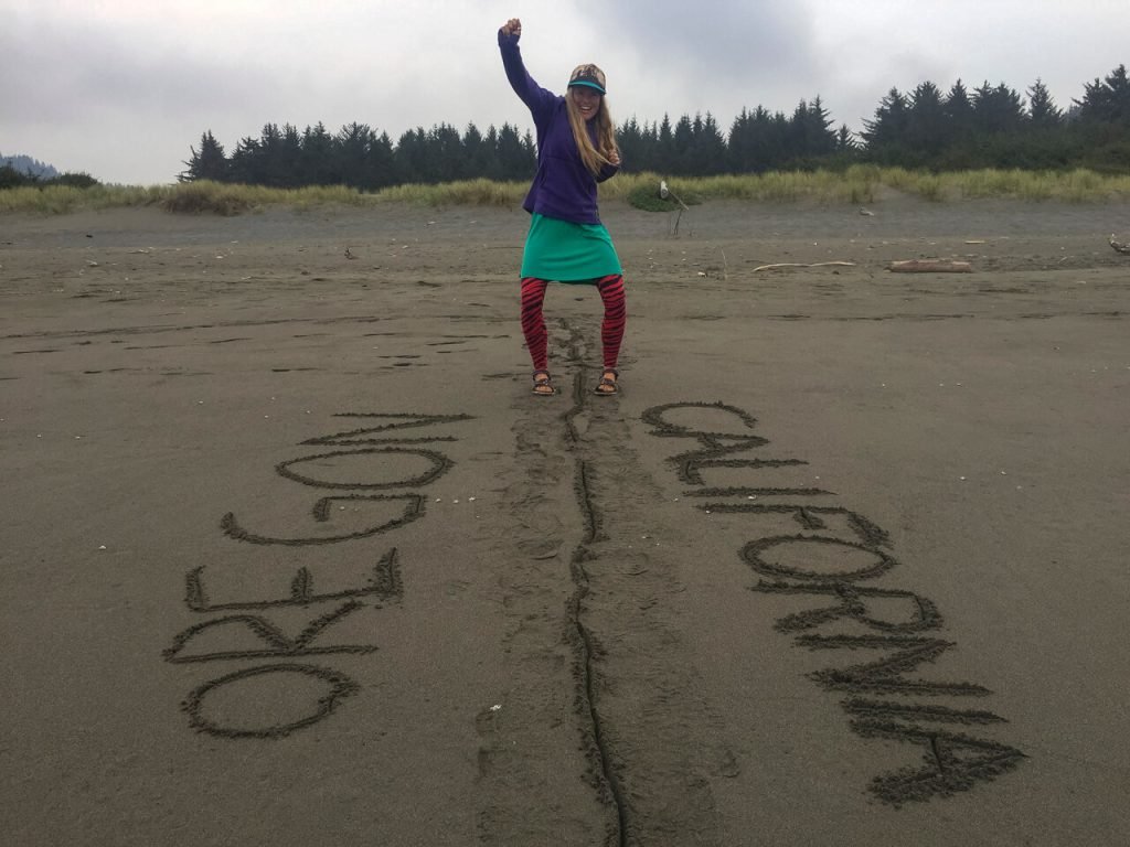 The end of the Oregon Coast Trail with a woman with one foot in each state.