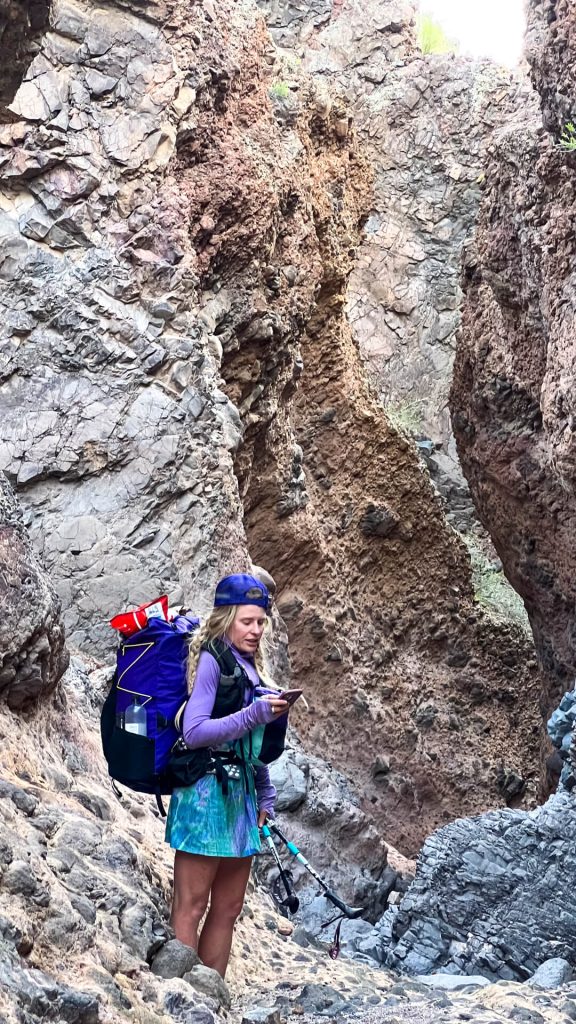 Woman backpacker in a canyon looking at maps on her phone.