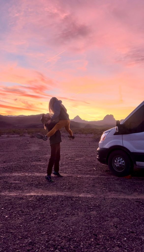 A van life couple jumping in the sunset in the desert during winter van life.