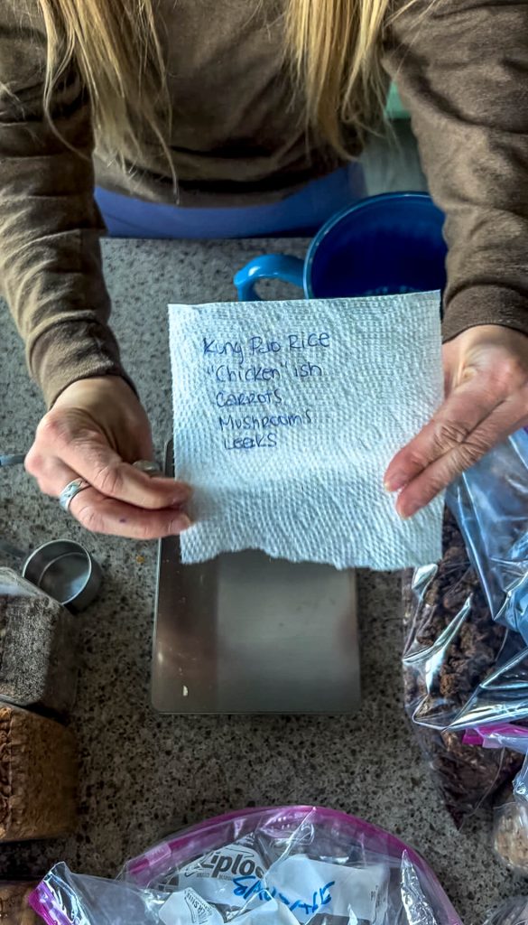 Woman holding a piece of paper towel up with a recipe written on it.