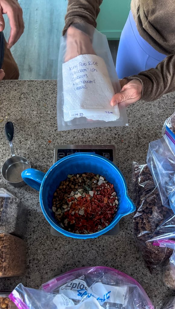 Woman placing a paper towel piece into a vacuum seal bag and a dehydrated Chinese food meal in a bowl in front.