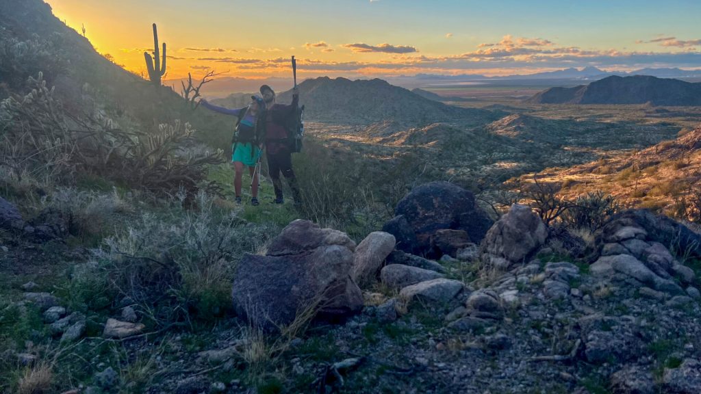 Two thru-hikers posing for a photo during a desert sunset.