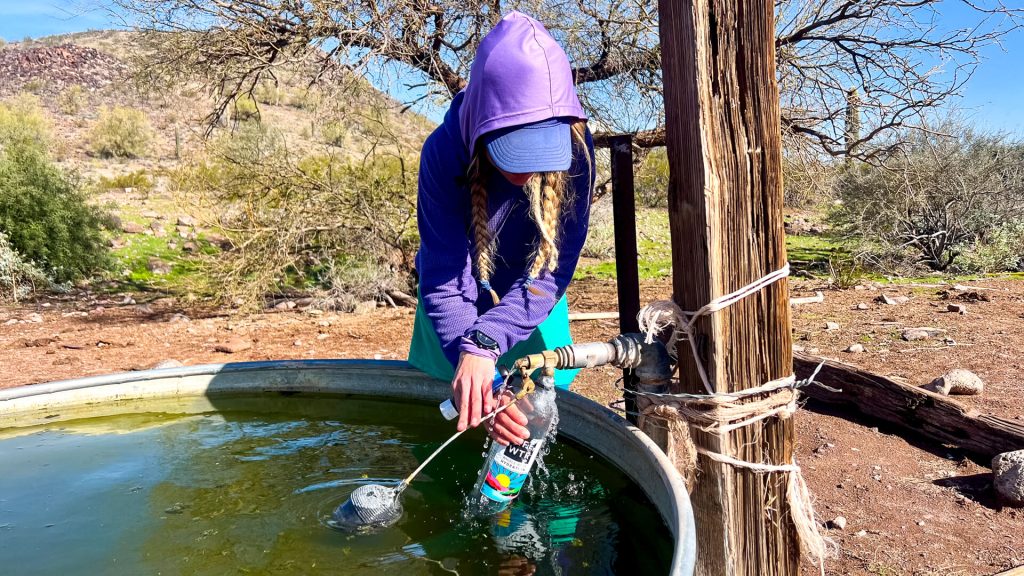 Woman getting water from a cow trough float value attached to a windmill.
