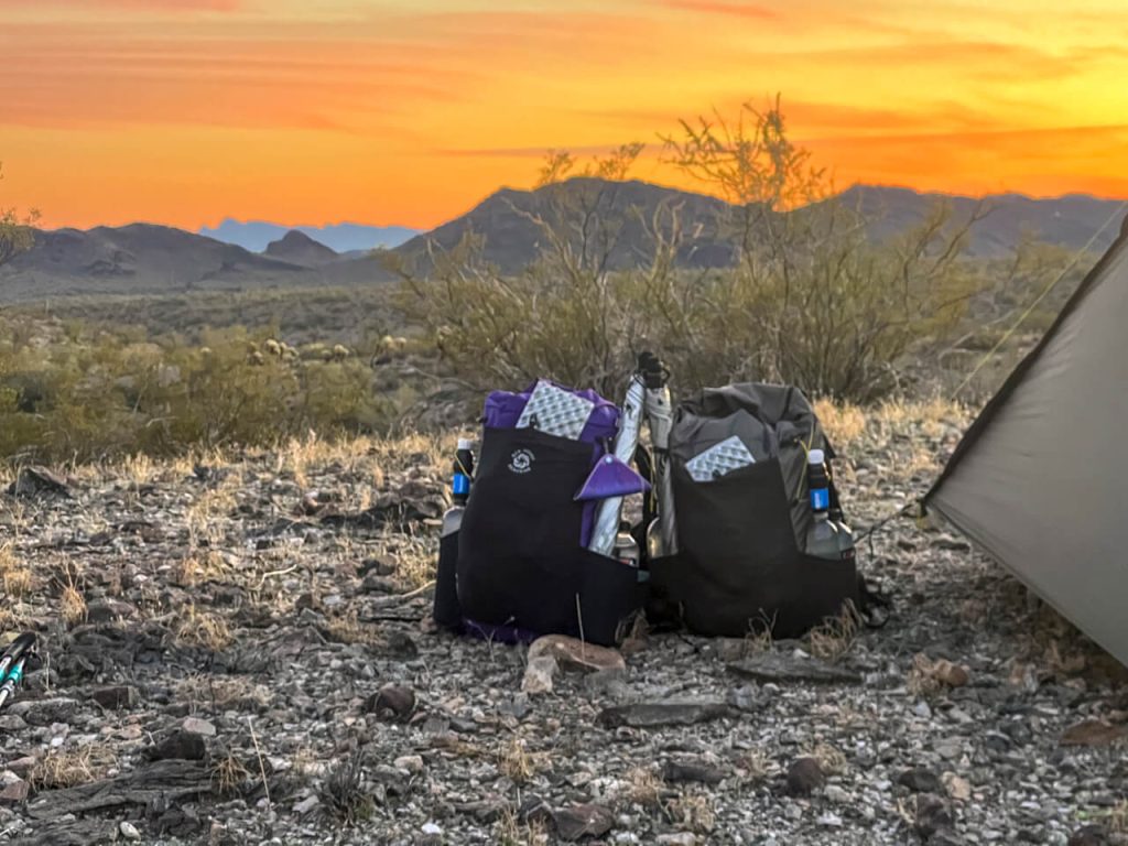 Two backpacks next to a tent in the bright orange Arizona Sunset
