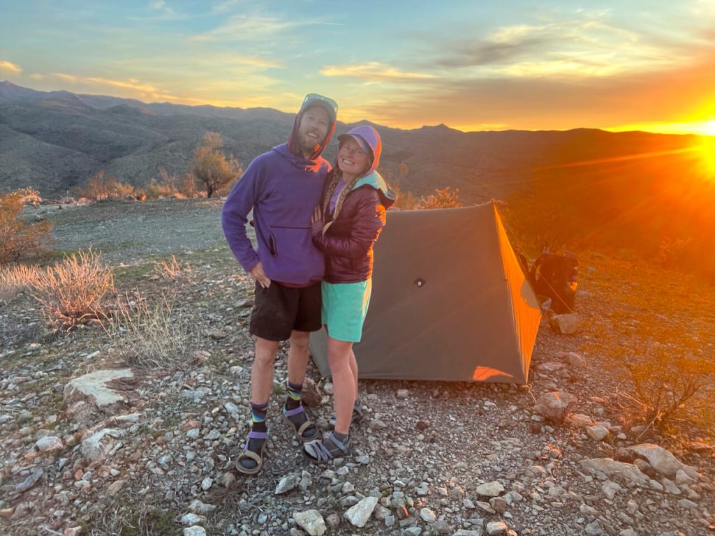 A thru-hiking couple with their tent at sunset.