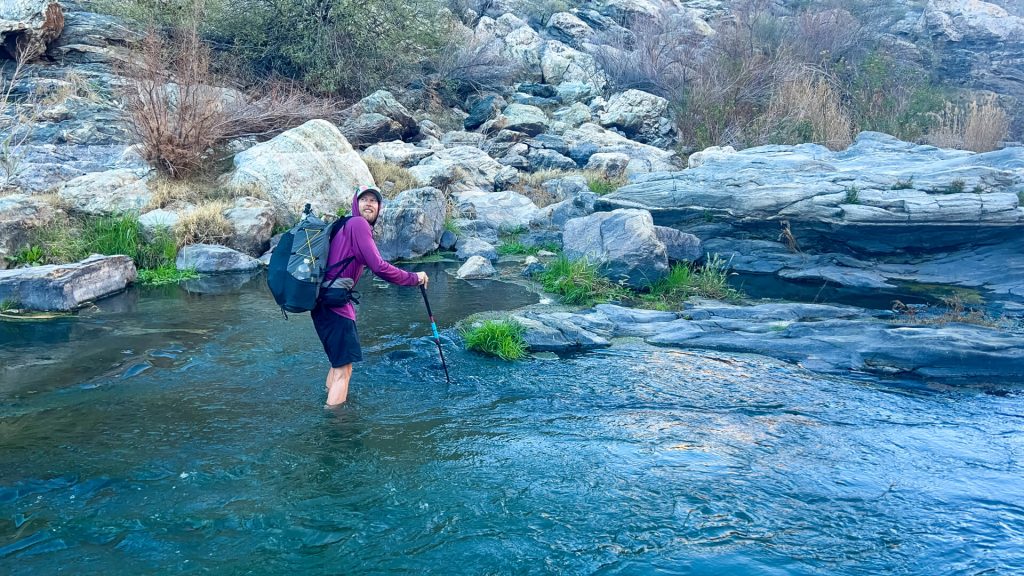 Thru-hiker is crossing a river with a backpack on.