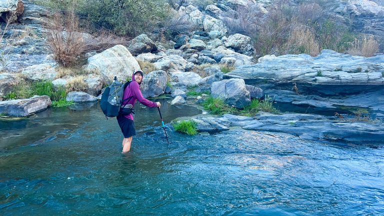 Thru-hiker is crossing a river with a backpack on.