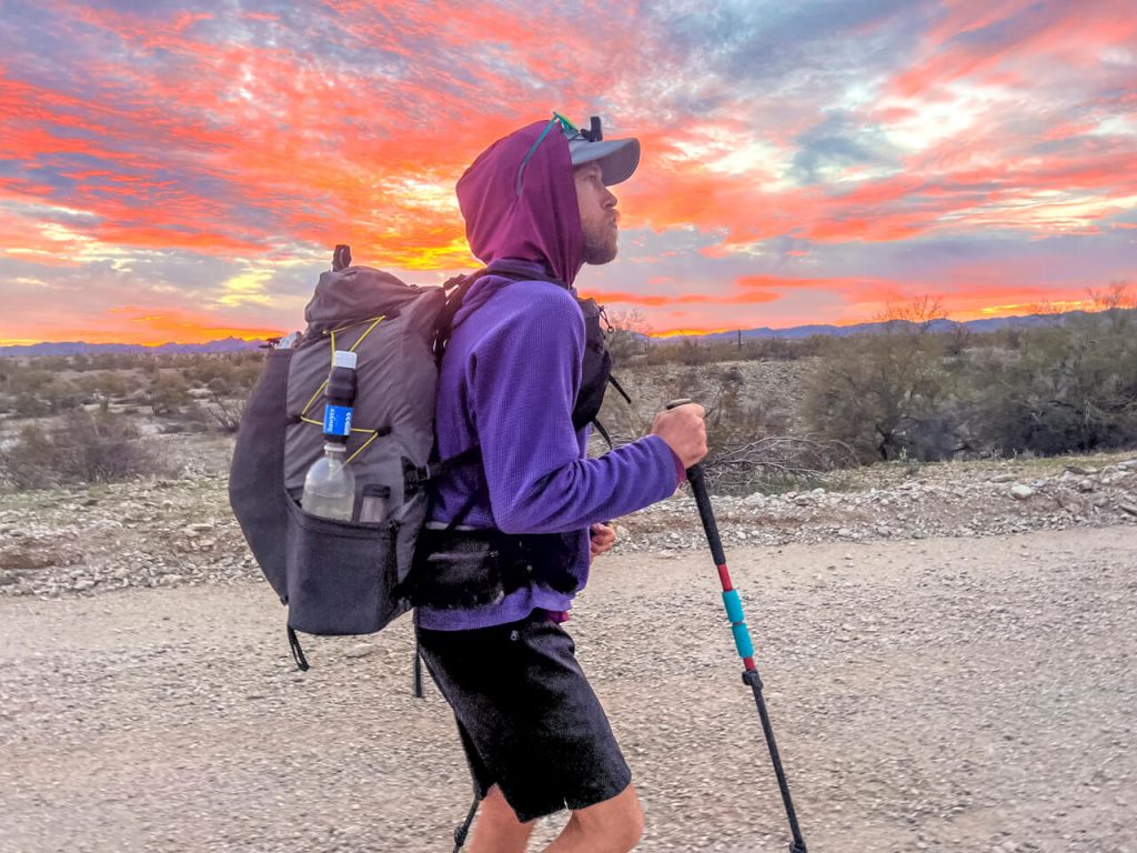 Thru-hiker walking with a bright sunrise in the background.