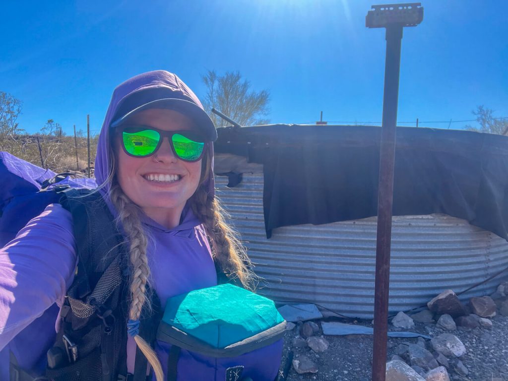 Woman thru-hiker in front of a desert water source.