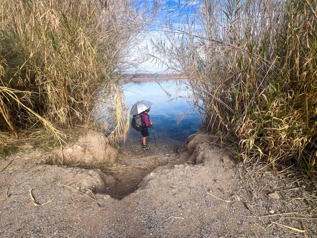 Thru-hiker stands near the Colorado River with an umbrella for shade.