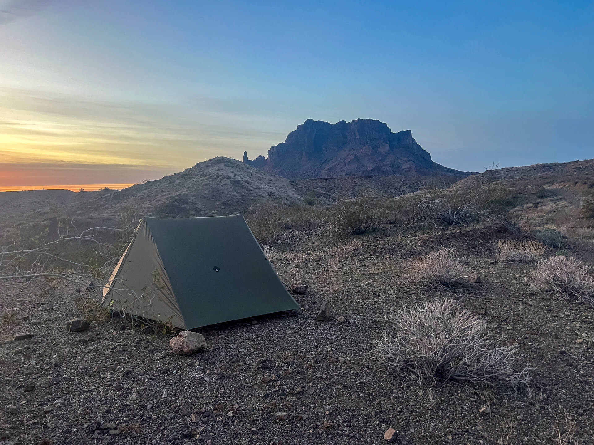 Tent setup at sunset with desert mountains in the background.