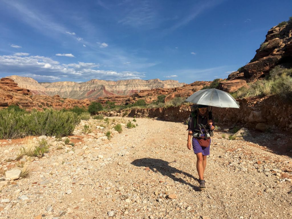 Thru-hiker using a backpacking umbrella as portable shade in the hot sun.