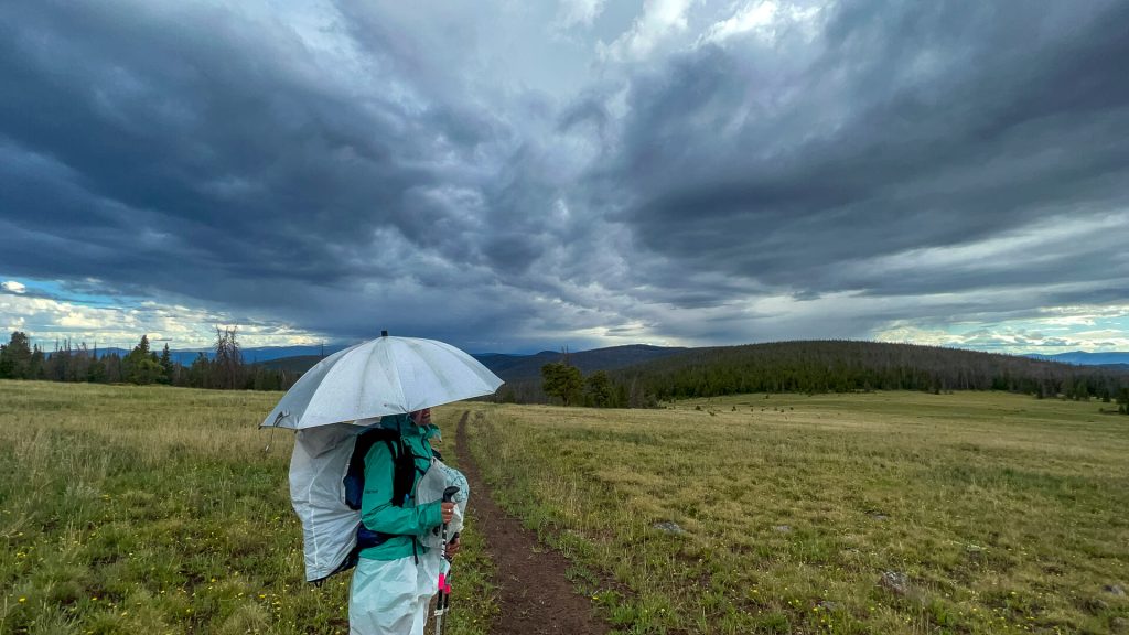 A thru-hiker with all her rain gear on looking back at an incoming thunderstorm.