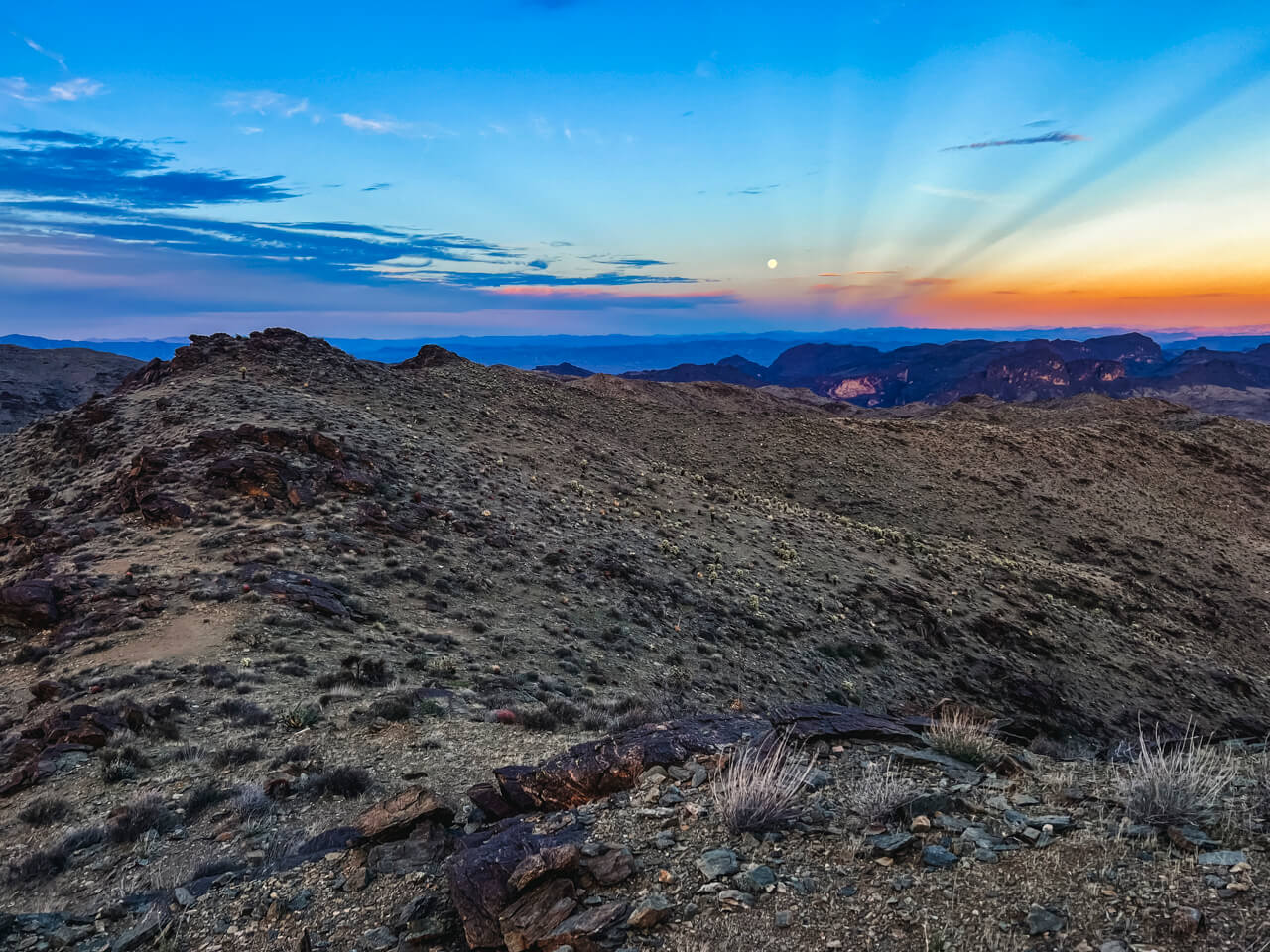 A desert sunset over a ridge with the moonrise.