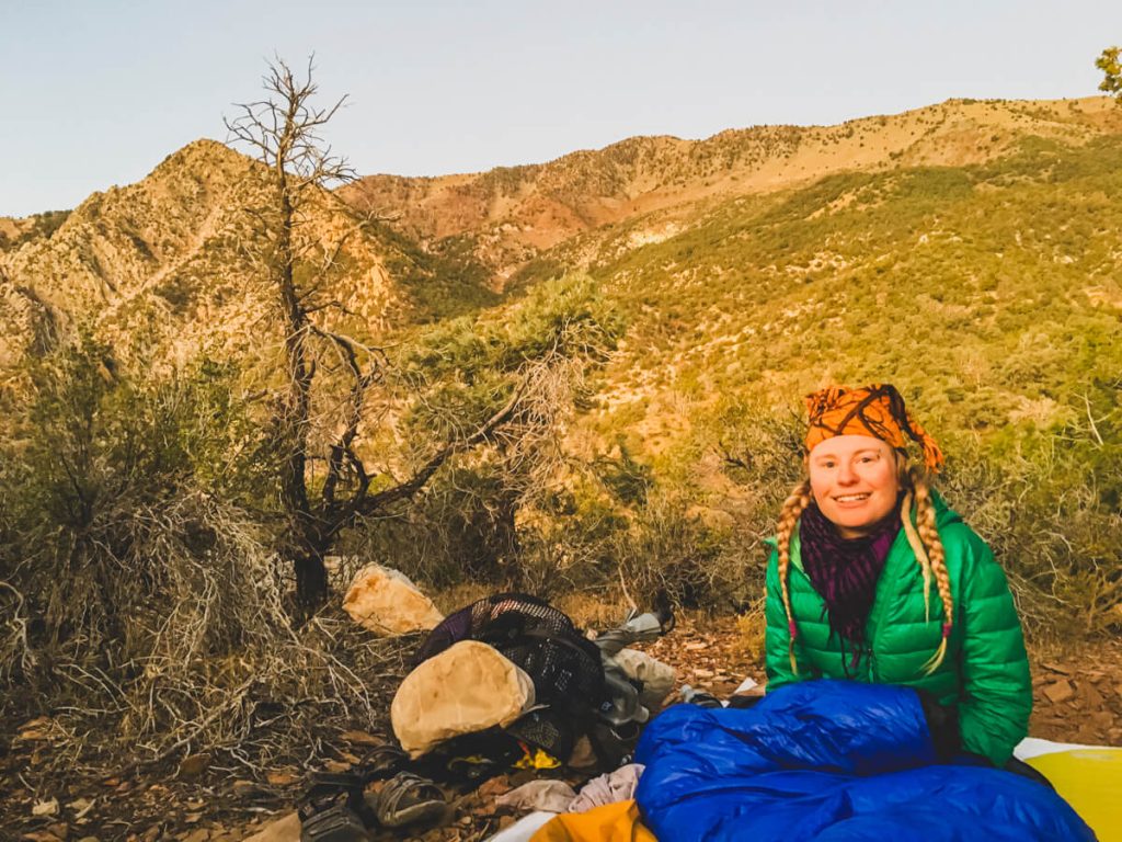 Woman backpacker waking up after cowboy camping on the side of a mountain.