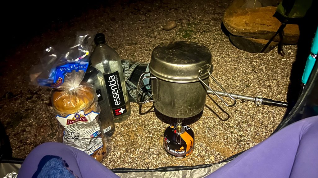 Backcountry cook system with a stove, fuel canister, cook set, and bagels.