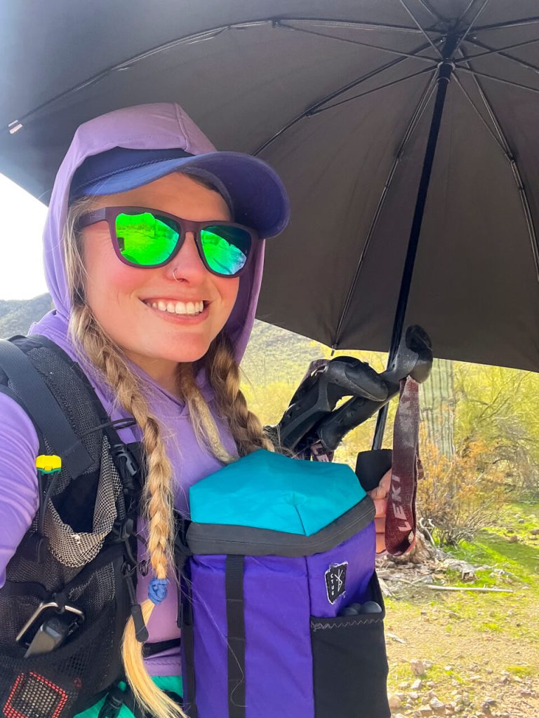 Woman thru-hiker with a camera front pack hiking with a sun umbrella.