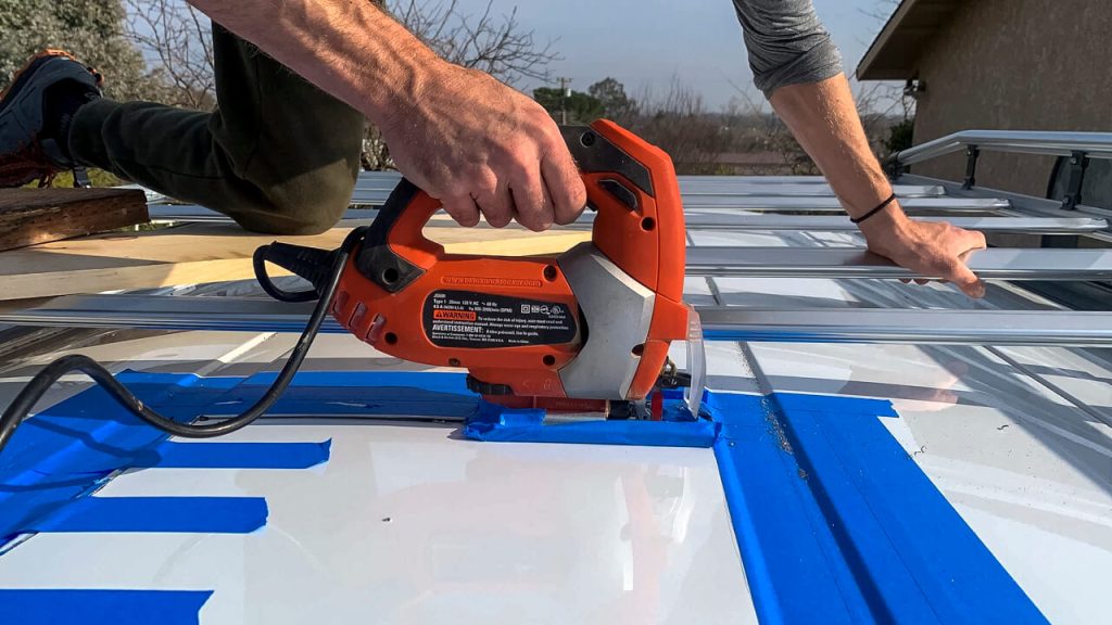 Painter's tape surrounding the cut line and a jigsaw cutting a square hole for the MaxxAir Fan.