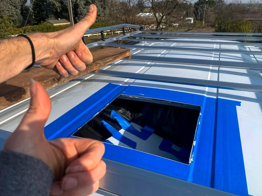 A van couple giving thumbs' up to the hole they just made in the roof of their van.