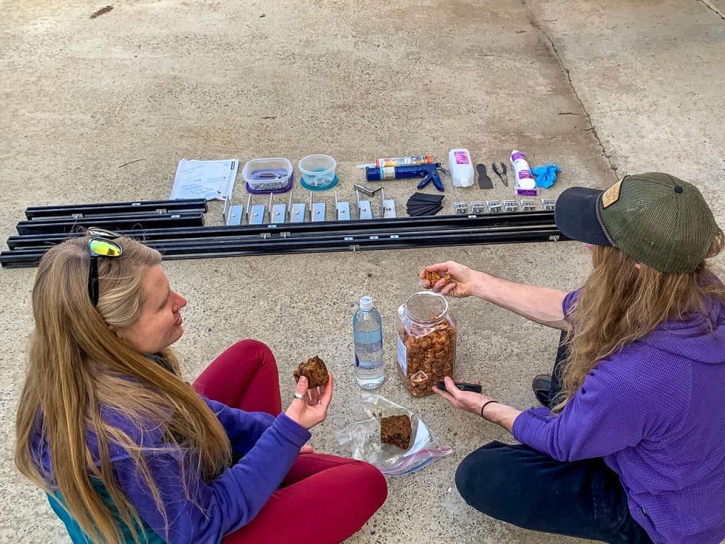 The Prime Design Alurack parts laid out on concrete and a van couple having a snack.