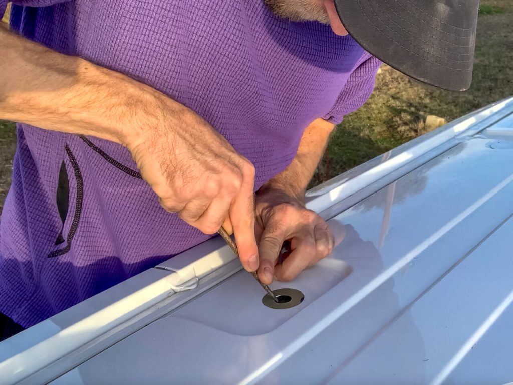 Man using a metal file to widen the bolt hole so a bolt can screw in without stripping. 