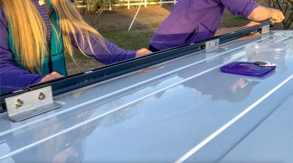 A van couple aligning two channels for their van roof rack while assembling it.