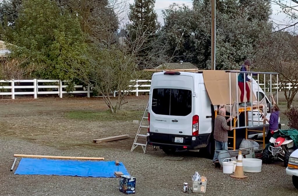 Three people hoisting up a van roof rack onto the top of a van.