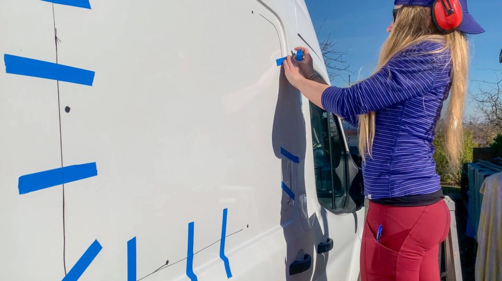 Woman adding painter's tape to hold the sheet metal in place as the hole is cut.