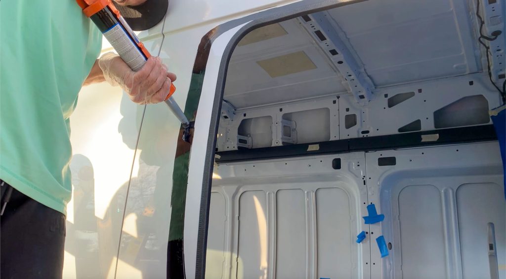 Man adding the urethane in preparation for a van sliding window.