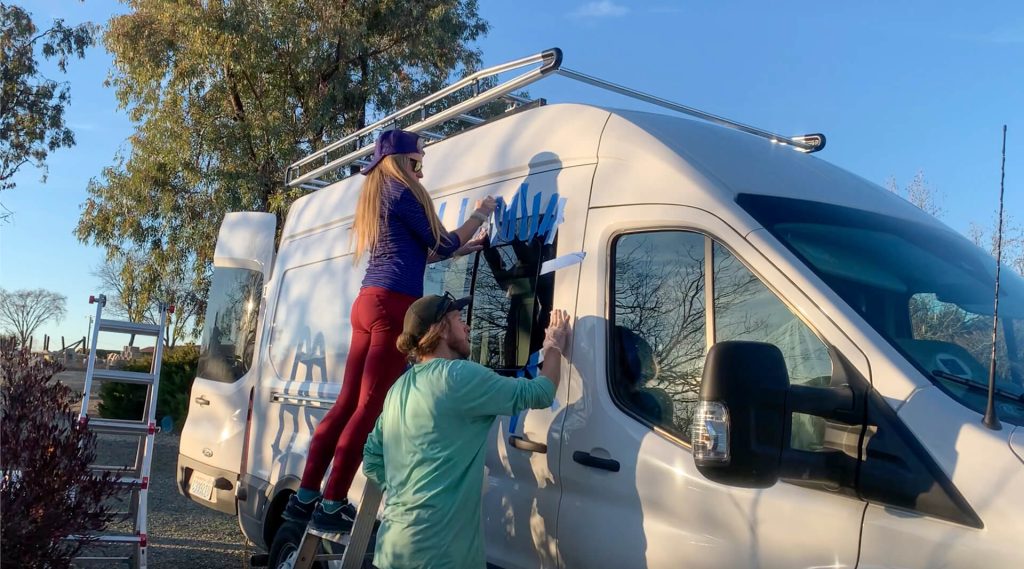 A van couple adding painter's tape to hold their van sliding window in place while the urethane dries.