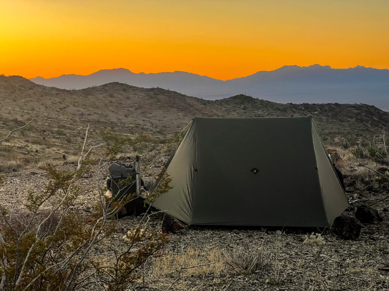 Desert sunset campsite with a tent and backpacking pack.
