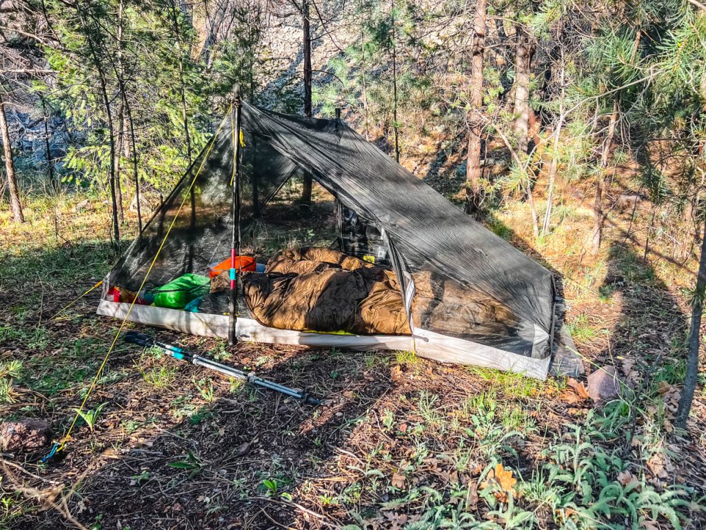 A net tent set up in the forest with camping gear inside.