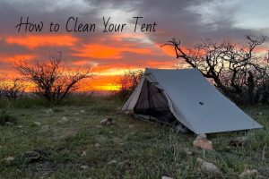 A tent set up in a desert sunset with text on how to clean a tent.