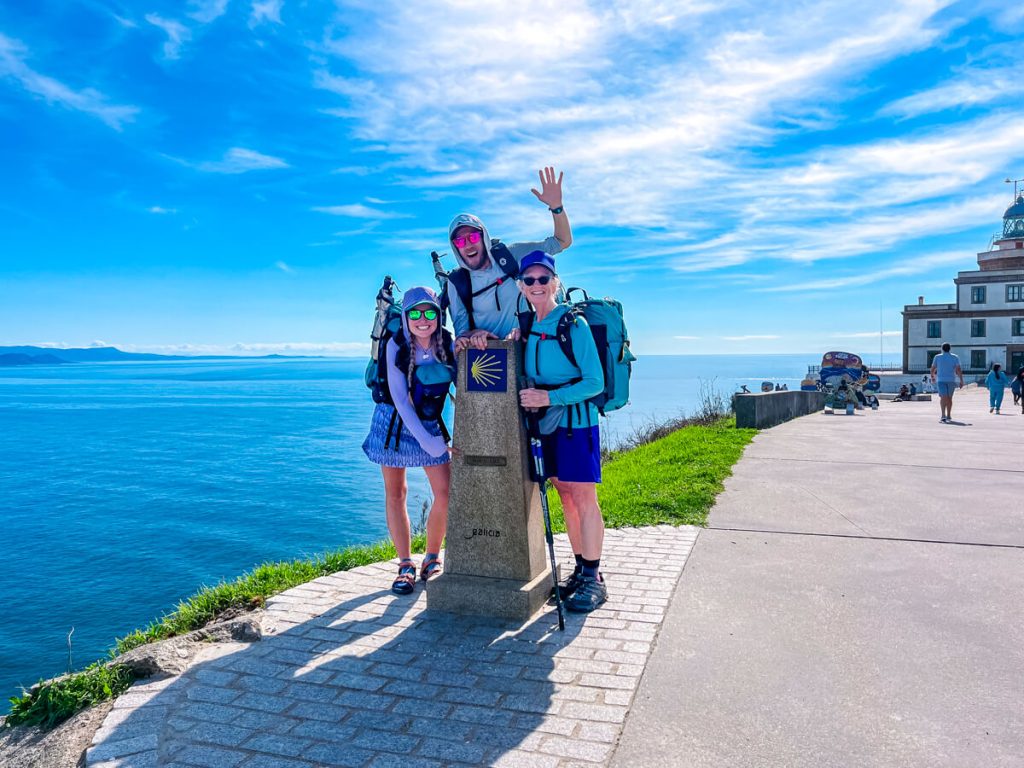 Three pilgrims at the Kilometer 0 marker in Finisterre, Spain by the lighthouse at the end of the Camino Finisterre.