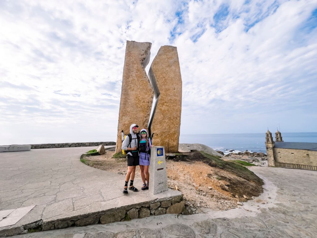 Two hikers at the Kilometer 0 marker and oil spill monument in Mux&iacute;a, Spain at the end of the Camino Mux&iacute;a.
