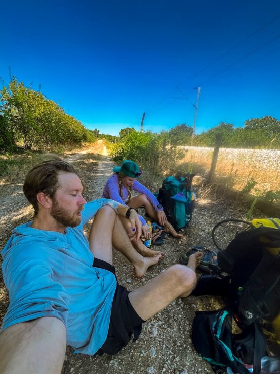 Two thru-hikers taking their shoes and socks off at a break in the shade to avoid blisters while hiking.