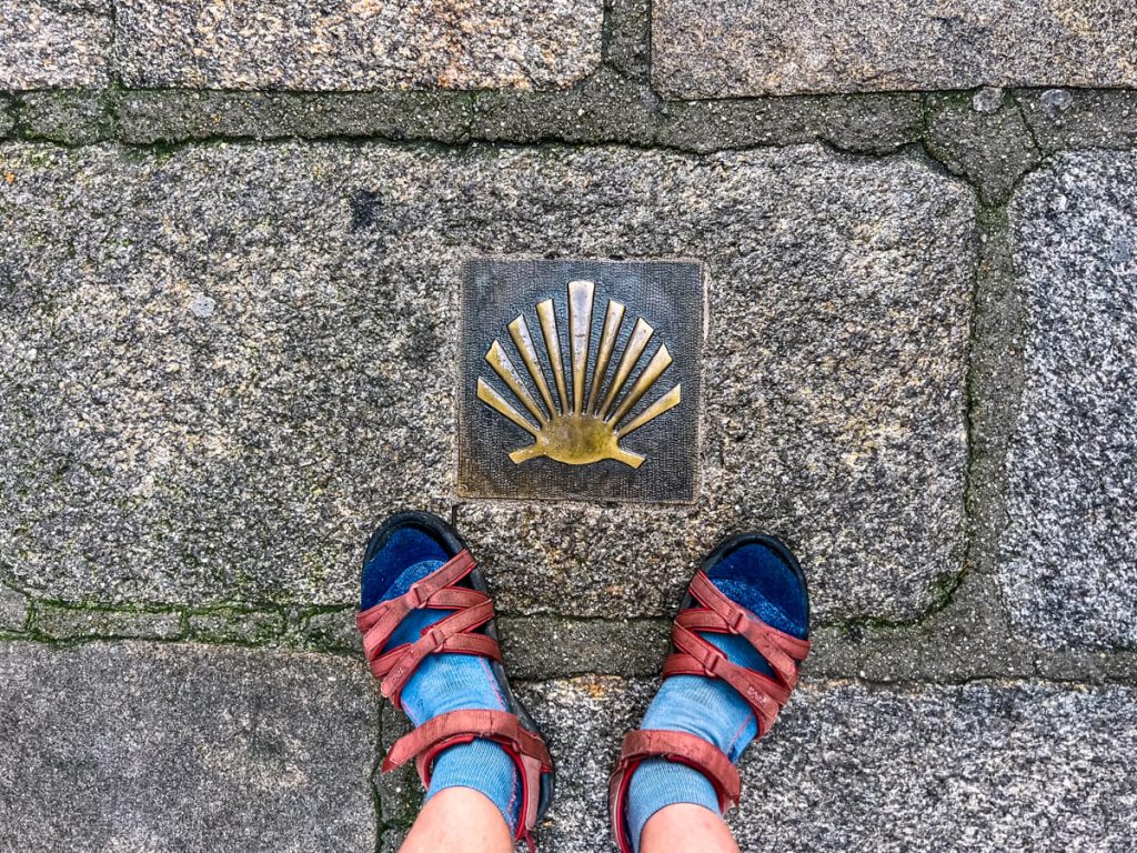 Camino marker on the ground with feet.