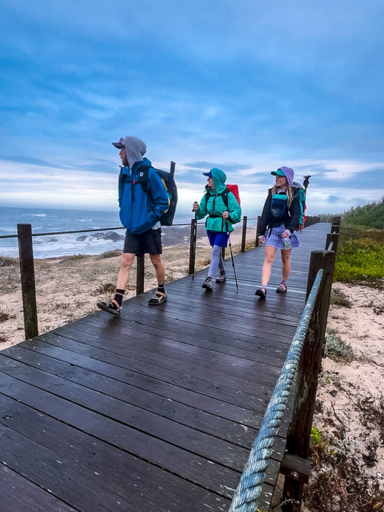 Three camino pilgrims walking on the boardwalk on the Portuguese Camino coastal route.