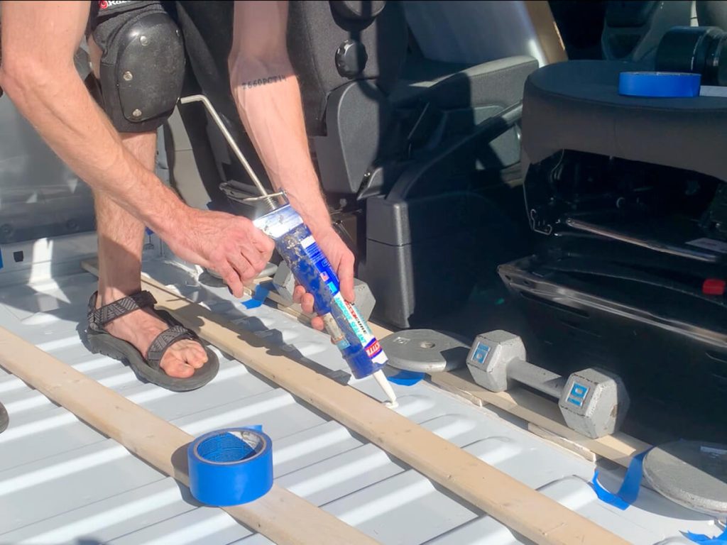 Using marine adhesive to install furring strips to the van's metal floor so the subfloor can screw into them while also providing space for insulation,