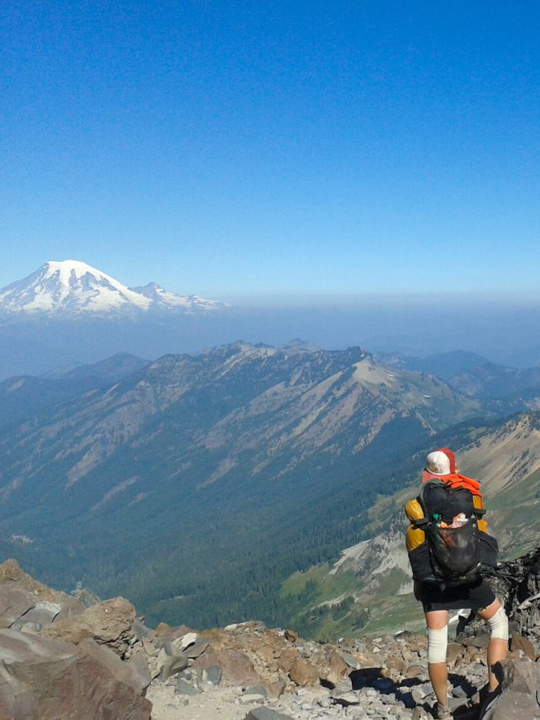 Woman thru-hiker on the Pacific Crest Trail looking at Mt. Rainer wearing the ULA Circuit backpack.
